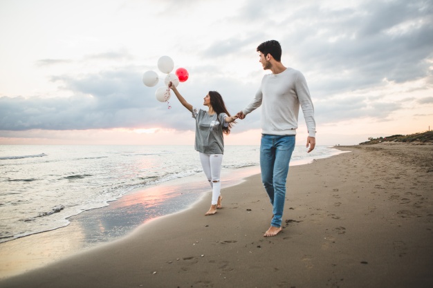 smiling-couple-walking-on-the-beach-with-balloons_23-2147595924
